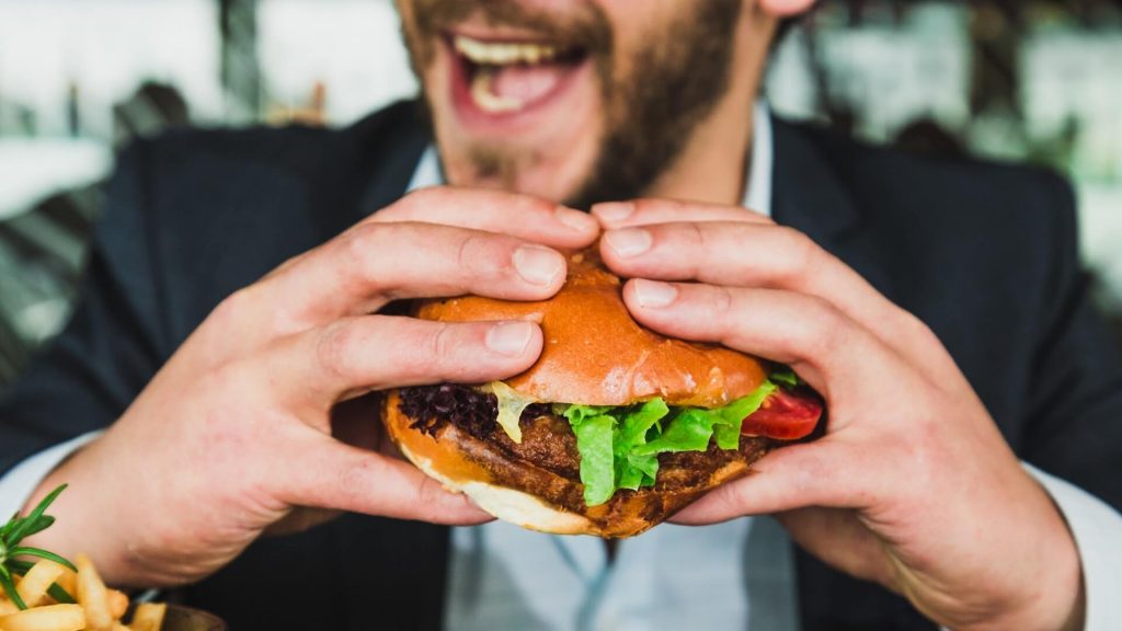 Image d'un homme savourant un hamburger, capturant le plaisir simple de profiter d'un repas.